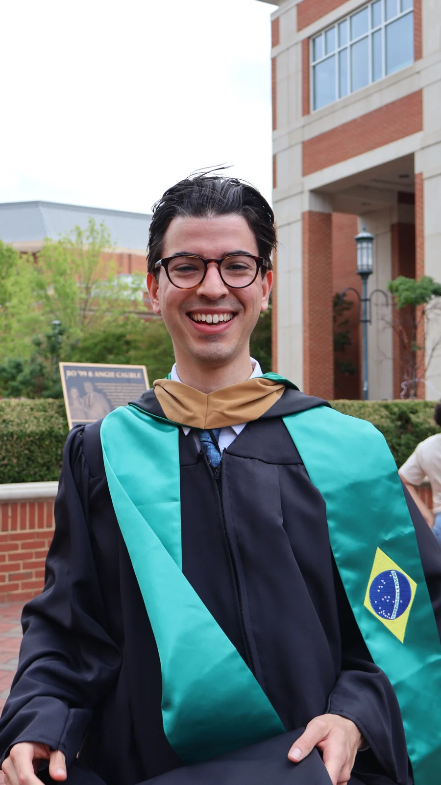 Felipe smiling in his graduation gown and Brazilian flag stole.
